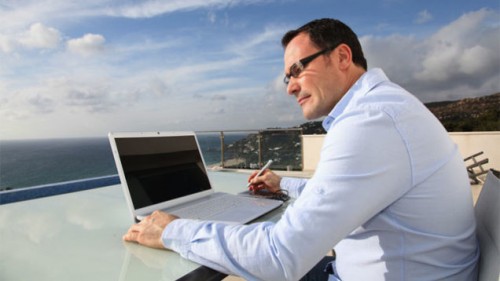 A man is outside and working on a laptop as part of his technomadic vacation.