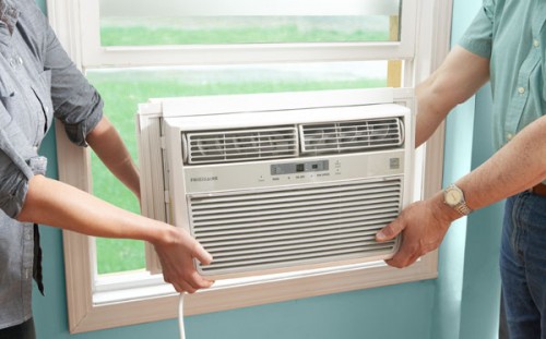 Two people installing an air conditioner into a window.