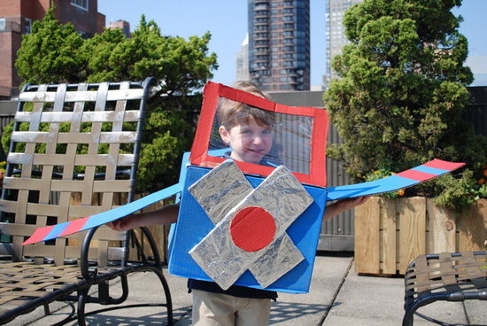 A boy is wearing a blue, red, and silver cardboard box airplane Halloween costume.