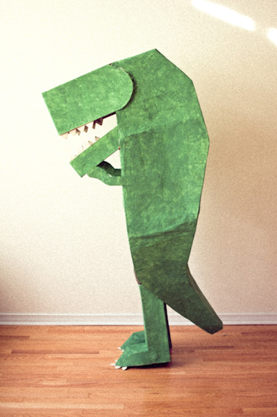 A person is wearing a green cardboard dinosaur Halloween costume.