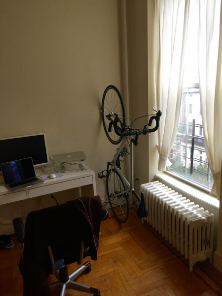 white and orange clug bike rack storing a bicycle vertically against a wall in an apartment home office
