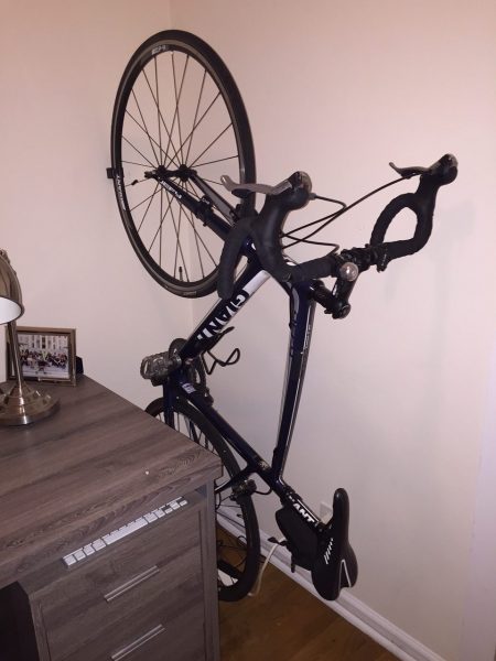 black clug bike clip storing a black bike vertically in a corner of an apartment between a desk and wall