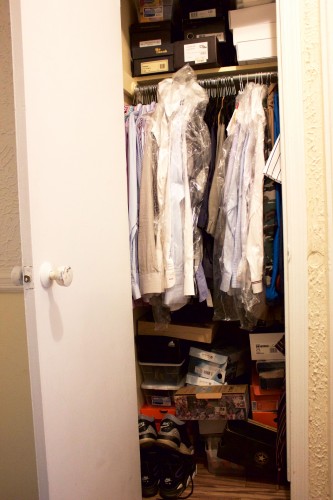 An unorganized bedroom closet stuffed with dress shirts and shoe boxes.