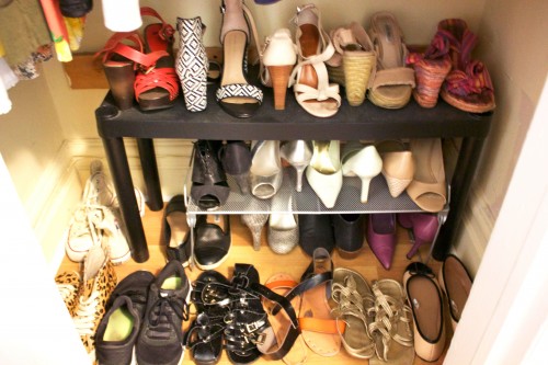 A tiny apartment's organized bedroom closet with shoes facing opposite directions on the floor, a rack, and table. 