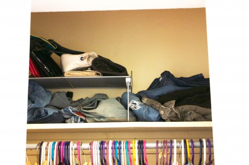 A tiny apartment's cluttered, unorganized bedroom closet with jeans scattered on a shelf.