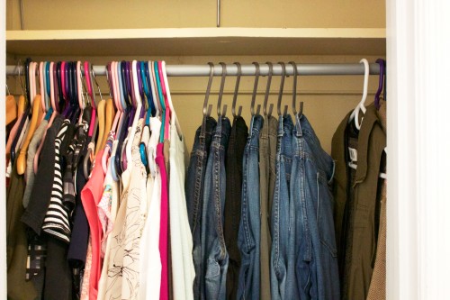 A clean, organized bedroom closet with jeans hanging on hooks and shirts on hangers.