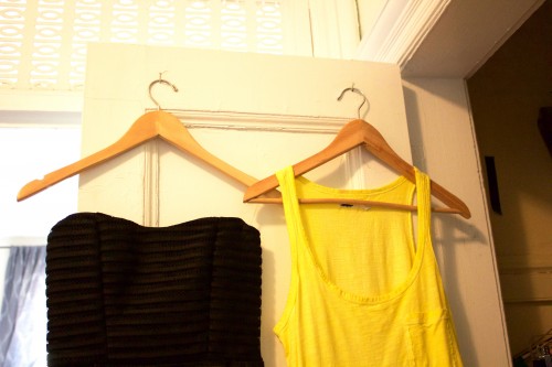 Black and yellow tops hanging neatly on wooden hangers on an organized bedroom closet's door.