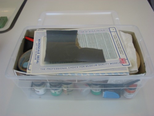 A clear storage container packed with small items from a modeling kit.