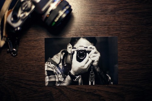 An old photograph of a guy taking a picture with a camera is lying face up on a table. 