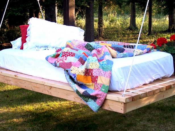 A DIY wooden shipping pallet bed hanging from trees.