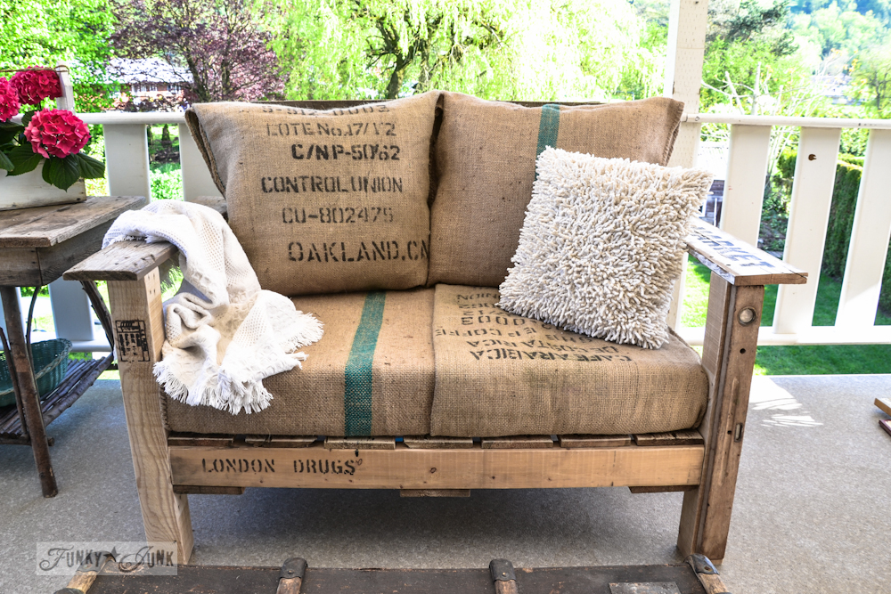 A cozy DIY wood pallet chair with a pillow and a throw blanket on top for comfort.