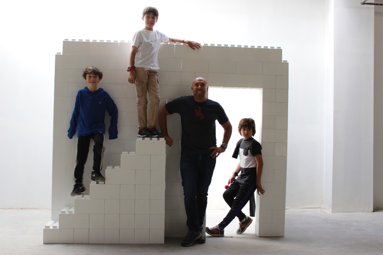 EverBlock Systems Founder and CEO Arnon Rosan is standing with his three sons in front of a white wall made of EverBlocks.