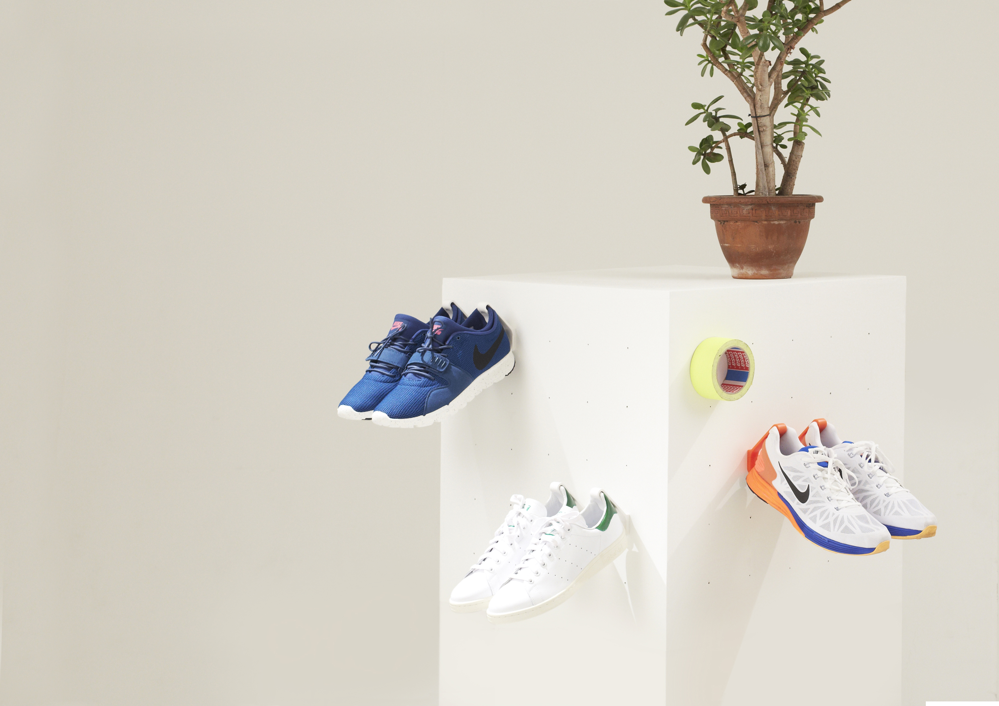 6 Staekler shoe storage hooks are mounted to a white column with a plant on top and hanging 3 pairs of sneakers.