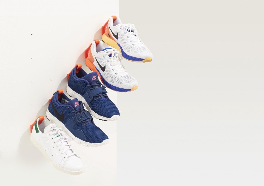 5 orange Staeckler shoe storage hooks are mounted diagonally to a white wall and hanging 5 sneakers.
