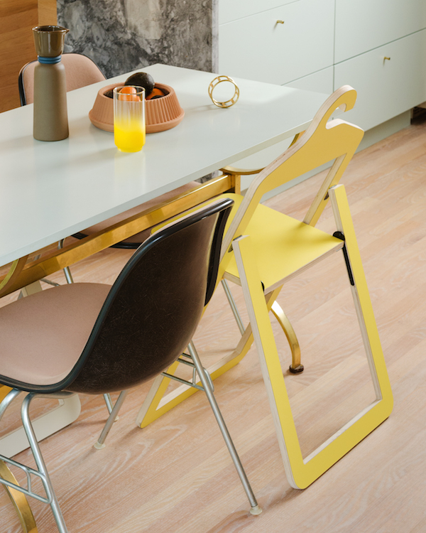 A black mid-century modern chair and an open yellow Umbra Shift Hanger Chair are at a white table.