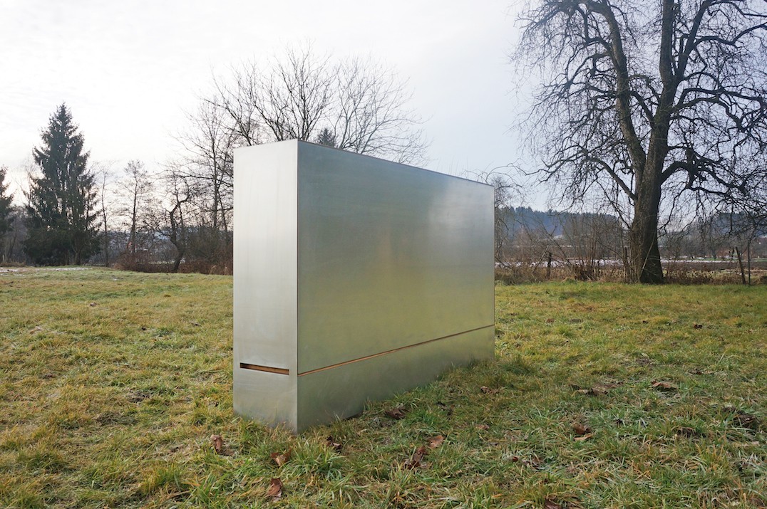 A closed Travelbox, a portable room in a box by JUUST Design, is standing in the grass.