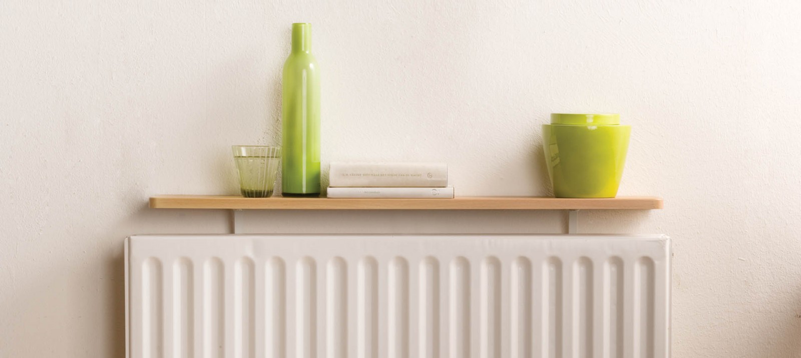 A drinking glass, decorative vase, books, and pots are stored on top of a radiator shelf kit from B!Organised.
