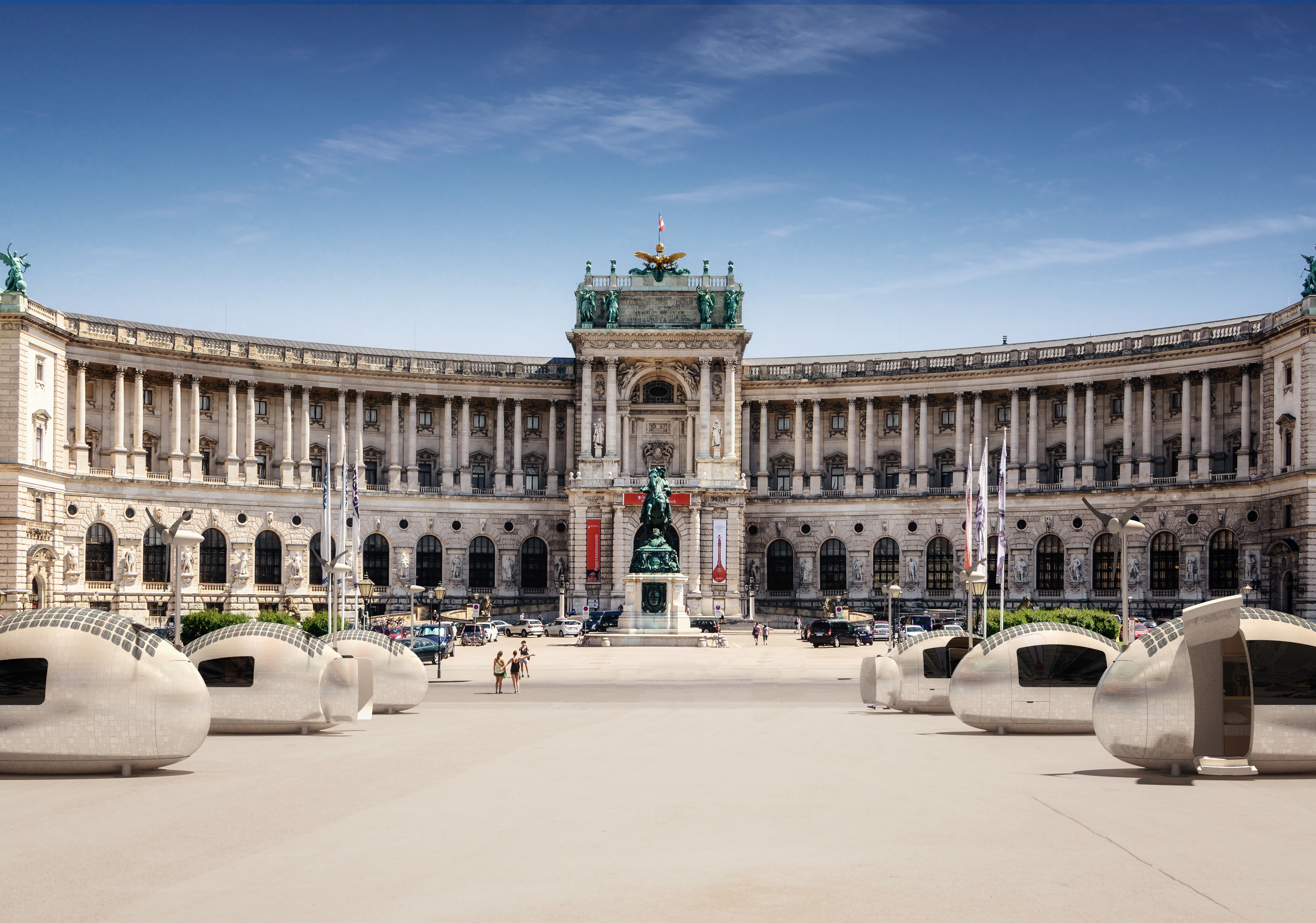 Six Ecocapsules are parked in front of a monument and building during the daytime.