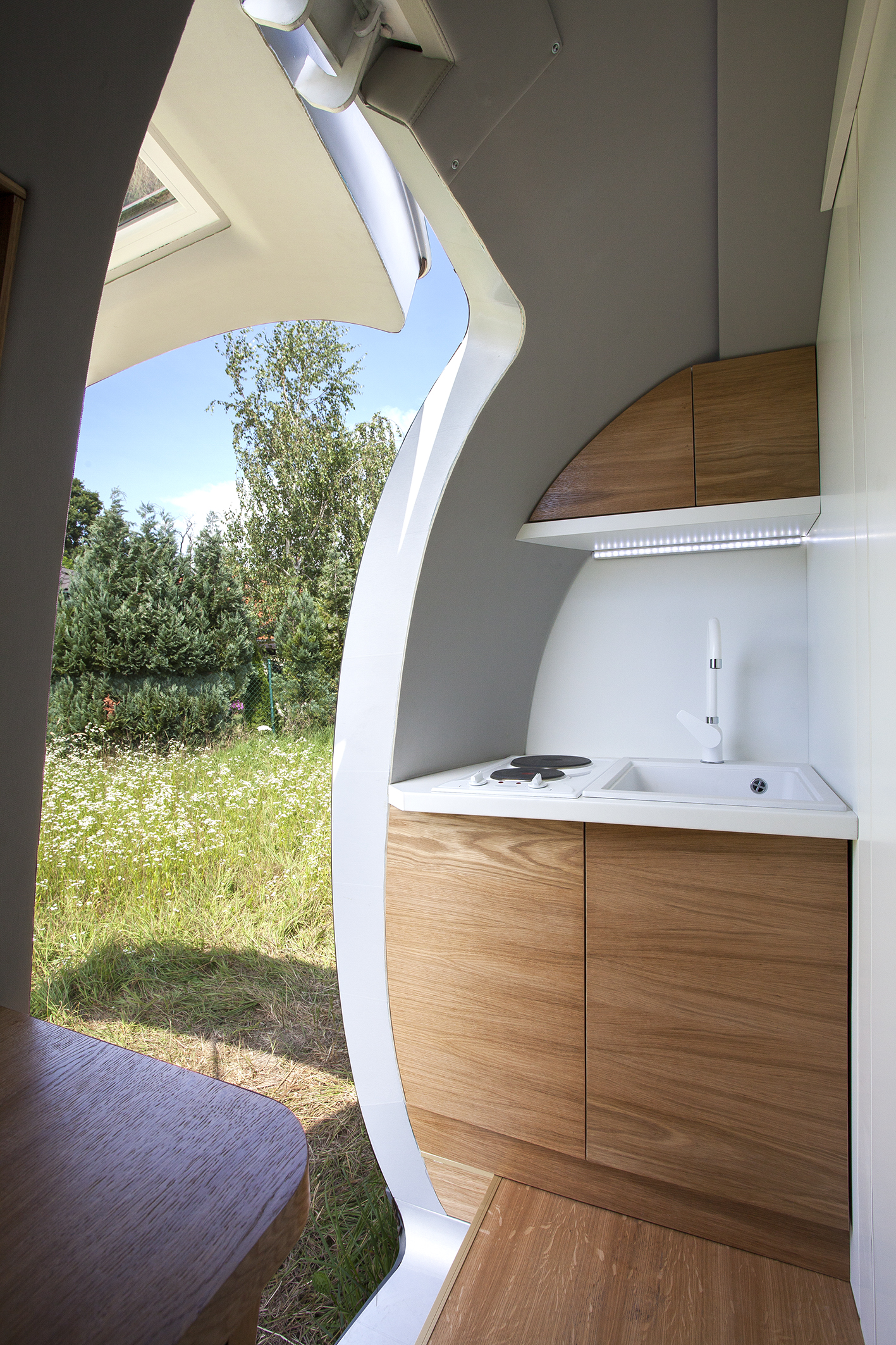 The Ecocapsule's kitchenette with a sink, two burners, and storage cabinets.
