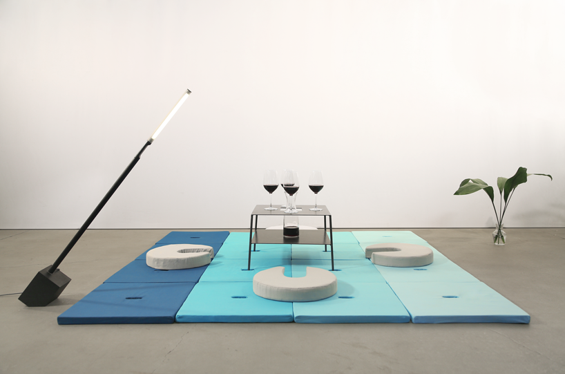 Square Pile cushions form tatami flooring, four circular Pile cushions form seats, and a metal table is storing four wine glasses and a carafe.