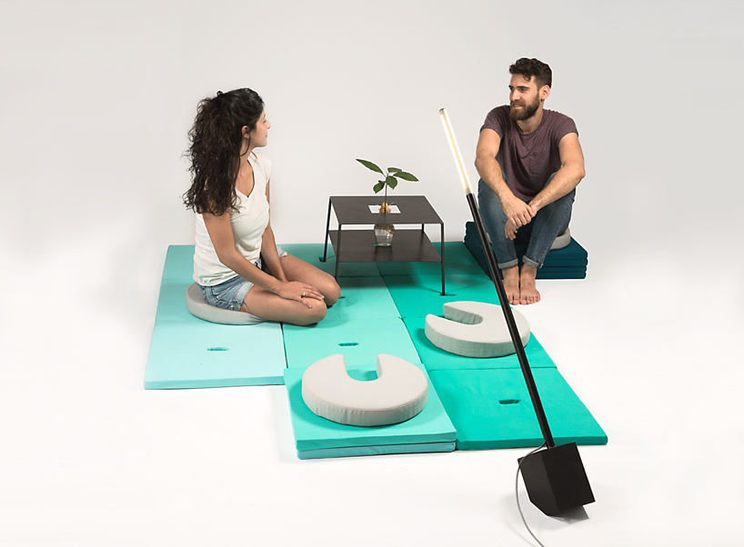 A woman and man are sitting on circular Pile cushions that are on square Pile cushions, all of which is arranged to form a romantic date spot with a small steel table that's storing a tiny plant.