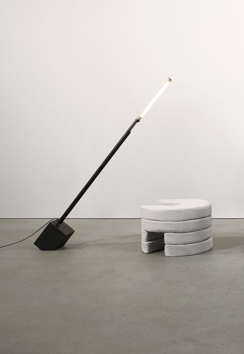 A thin black floor lamp is leaning over a seat made of circular Pile foam cushions.