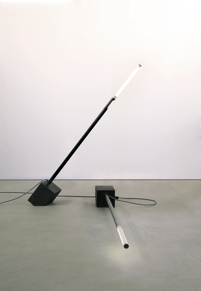 A skinny black Pile floor lamp is leaning over another floor lamp that's sleeping on the floor.
