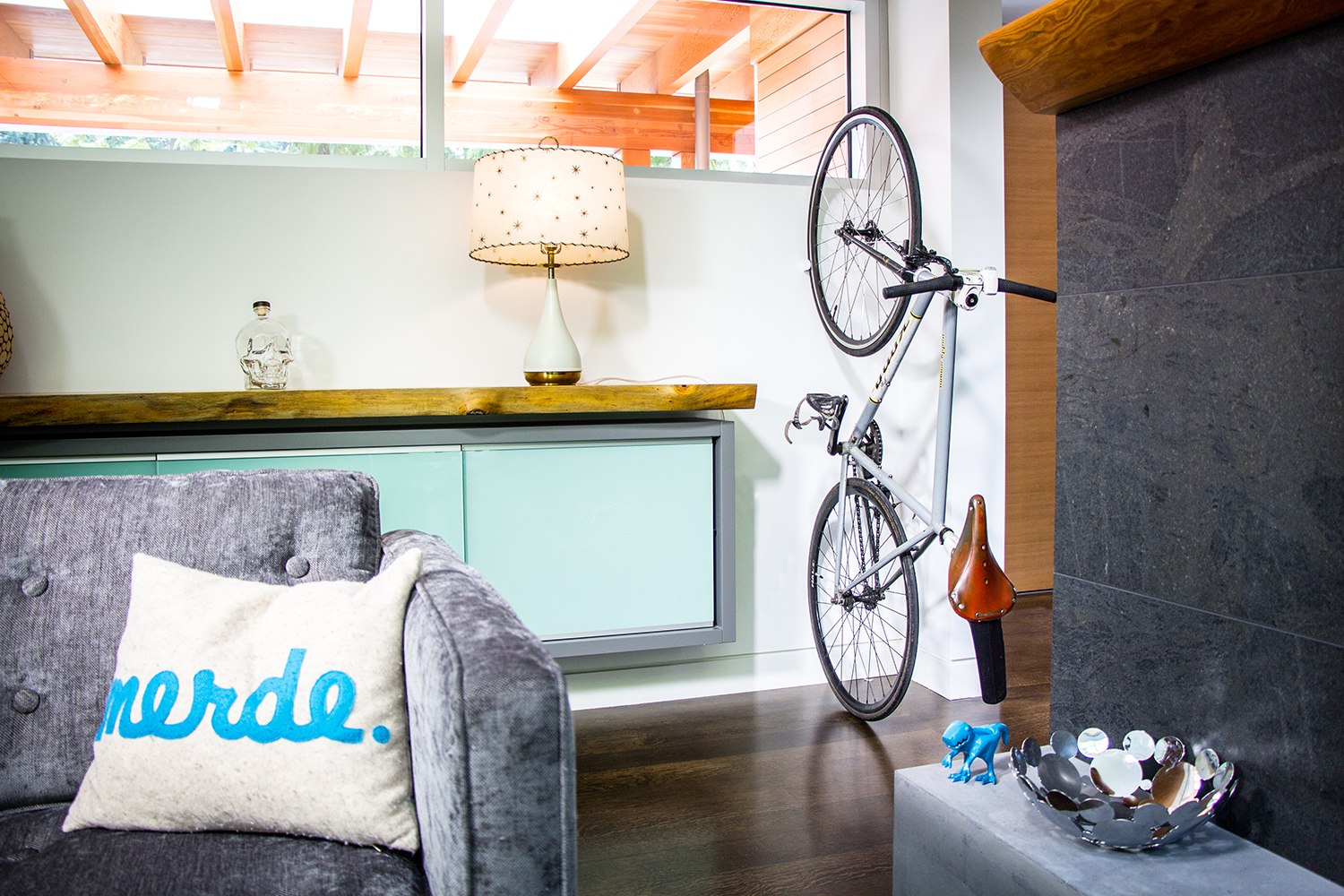 A white CLUG, which is a bike storage clip that mounts to a wall, is storing a bicycle upright in a small apartment.