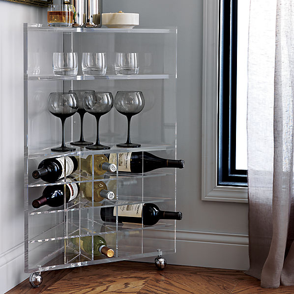 A clear space-saving SAIC Tonic Bar Cart from CB2, which is used for glassware, barware, and wine storage, is tucked into the corner of a small apartment.