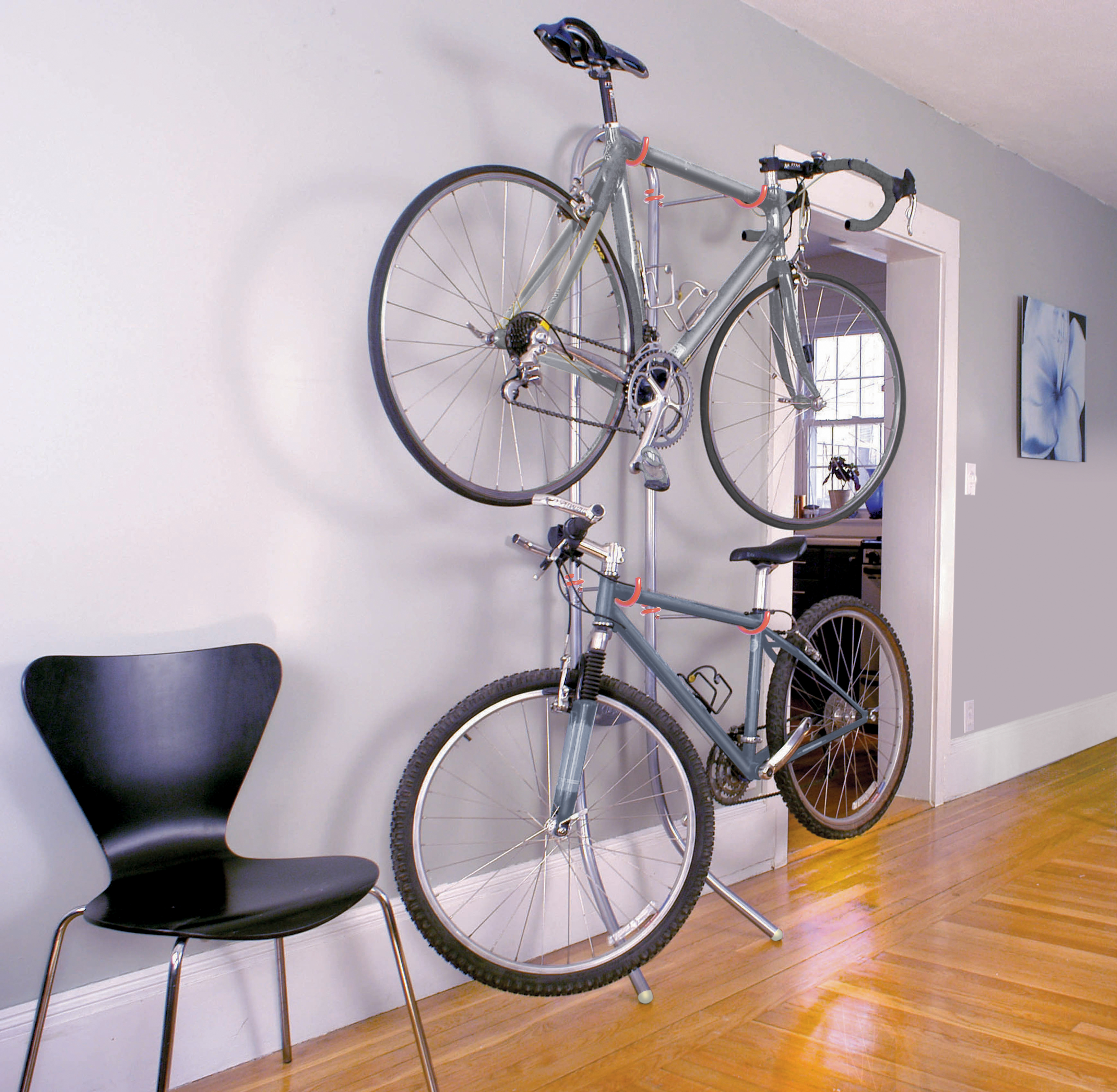 An Art of Storage Michelangelo Two Bike Gravity Storage Rack is leaning against a gray wall in a tiny apartment and storing two gray bikes.