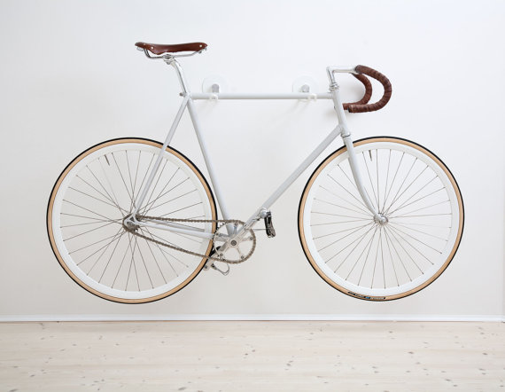 White Alexa Lethen Bike Hooks are mounted on a wall and storing a white bicycle in the air in a small apartment.