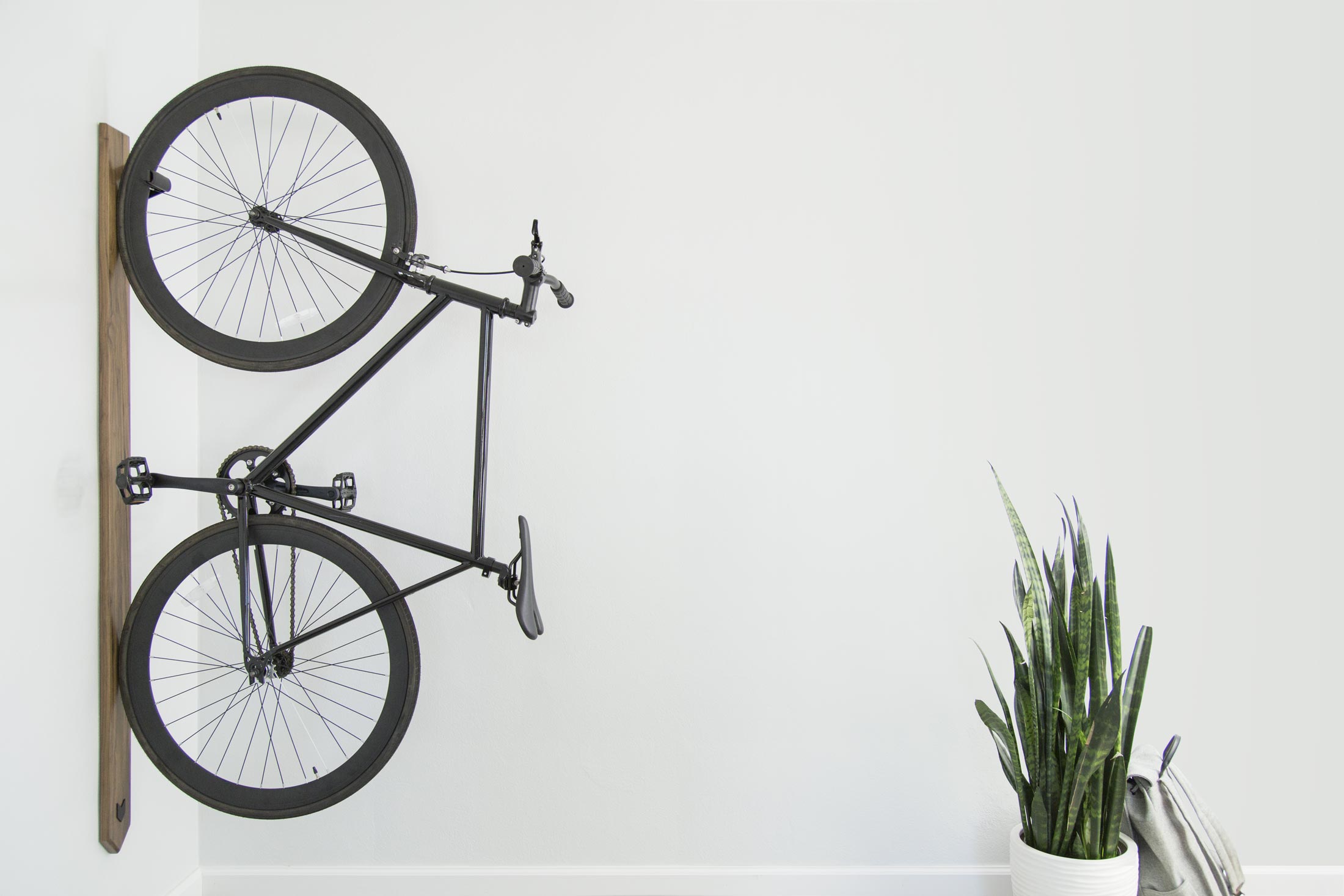 An Artifox Black Walnut Rack is mounted to a white wall in a tiny apartment and storing a black bike vertically.