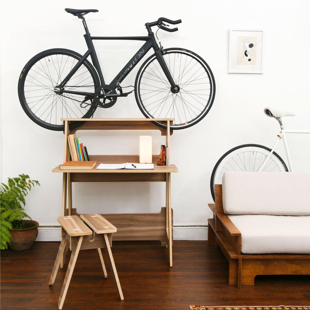 A wooden Chol1 DE5K bike storage desk is on hardwood floor in a clean tiny apartment and storing a black bike.