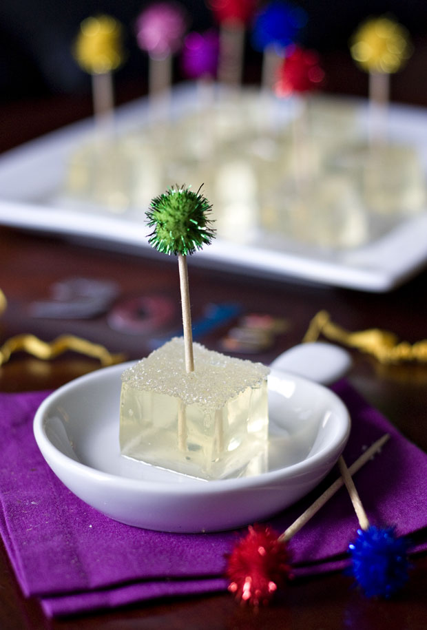 Homemade champagne Jello shots with a fancy toothpick in it that has a tiny green pom pom at the top.