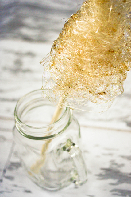 Homemade stringy golden cotton candy on a stick in a Mason jar with a handle.