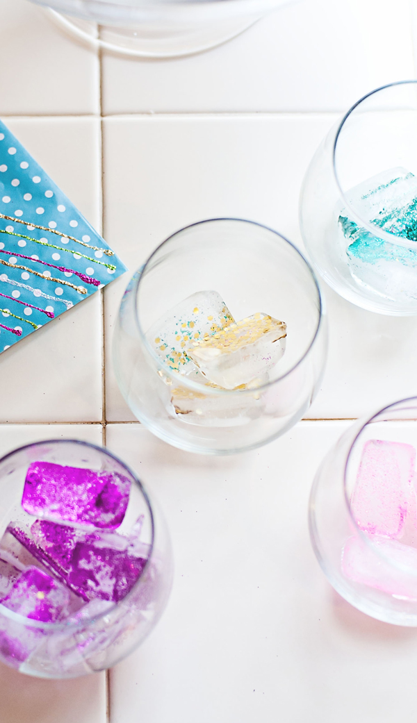 4 clear drinking glasses are full of edible various-colored DIY glitter ice cubes.