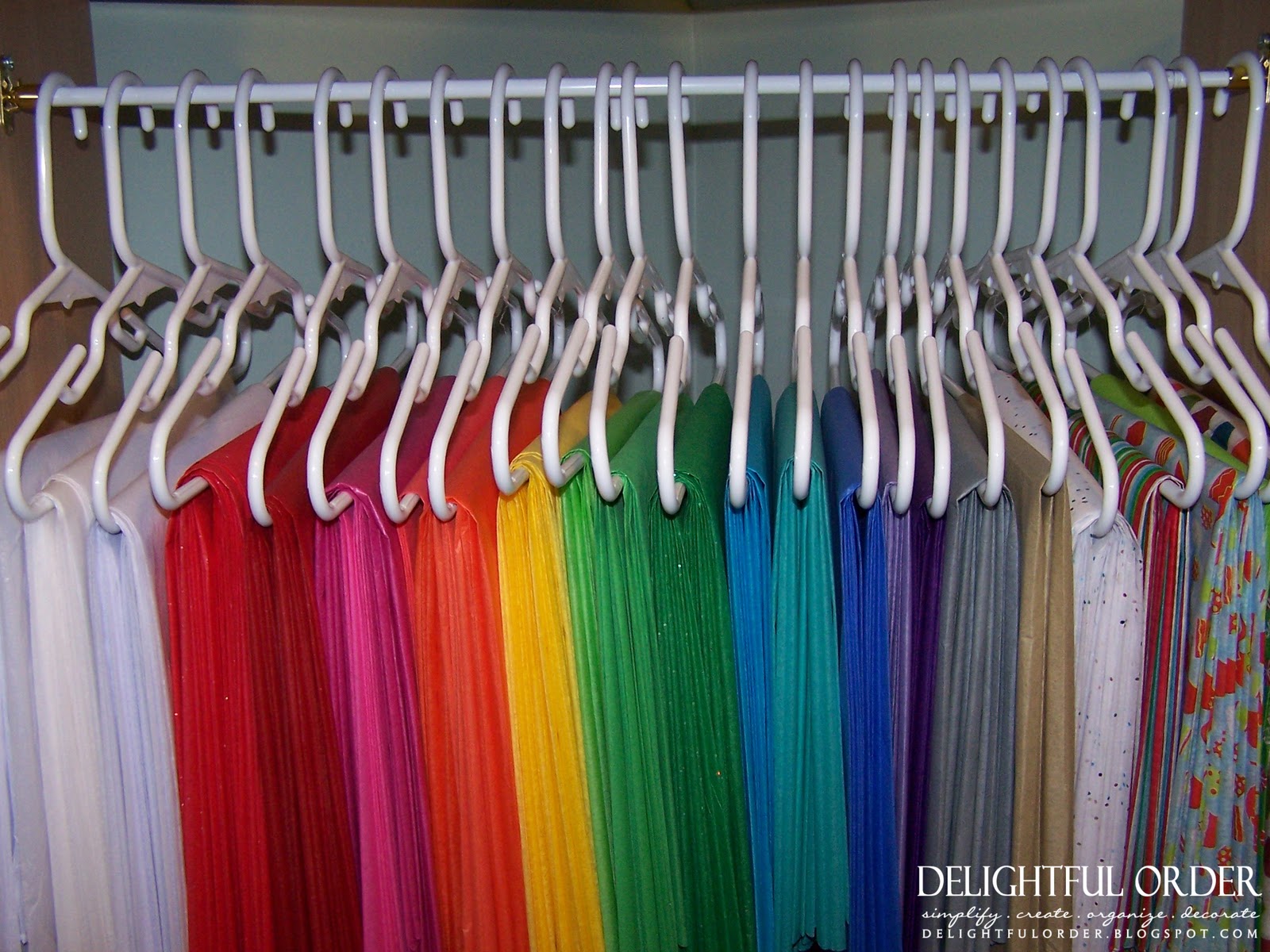 White clothes hangers are storing various colors of tissue paper in a closet.