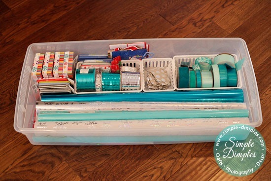 Holiday gift wrapping supplies are stored in organizing trays and a clear storage bin.