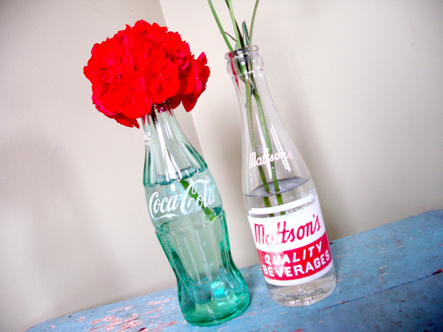 A vintage Coca Cola bottle and an old Mattson's soda bottle are storing flowers.