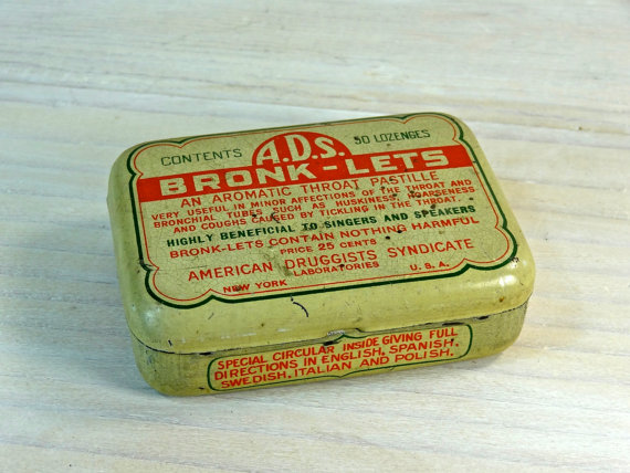A Bronk-Lets tin container used for medicine storage is on top of a wooden table.
