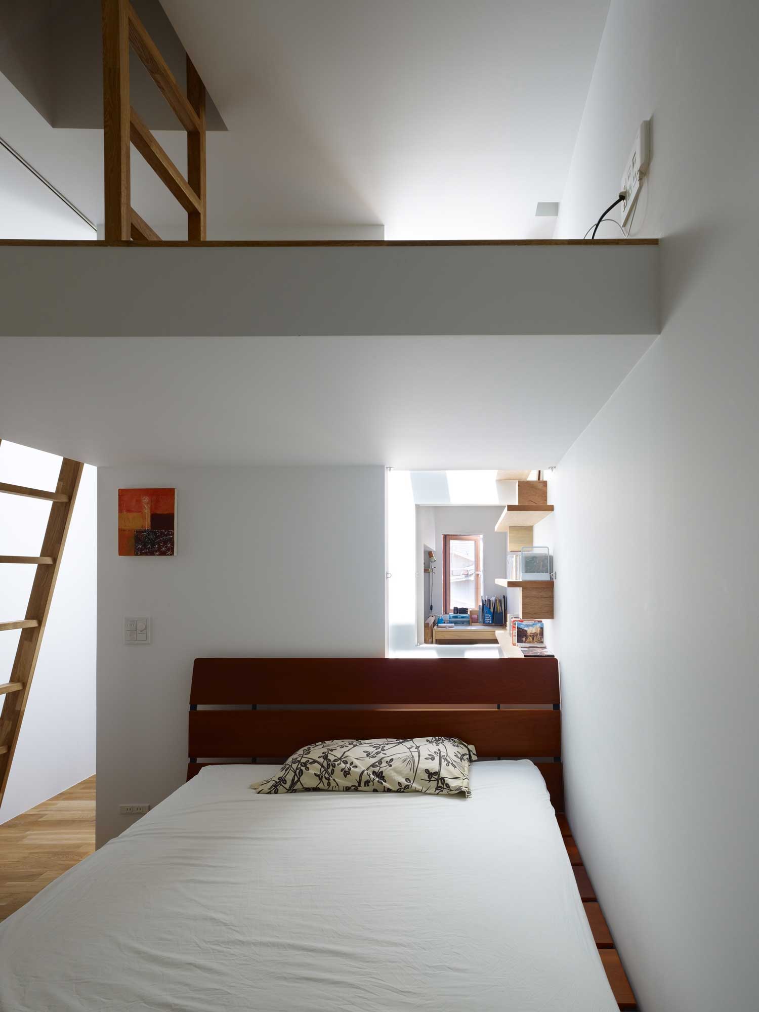 The white interior of a clean, organized, and minimally decorated small apartment that has storage shelves, a loft, and wooden furniture.