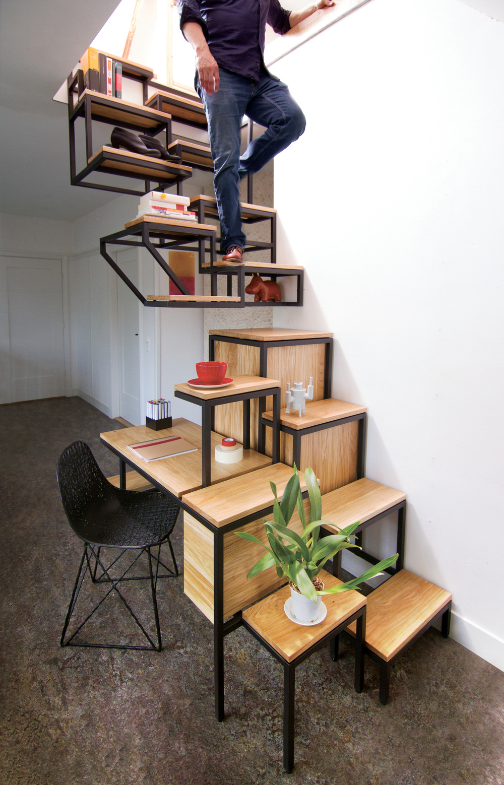 A man is walking down the Mieke Meijer Objet Eleve, a suspended staircase with storage, a desk, and a side table.