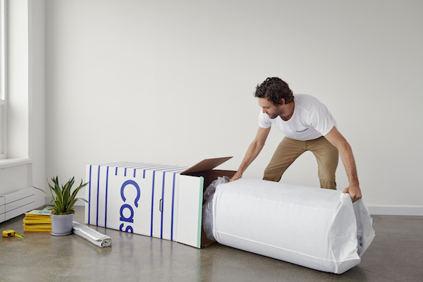 A man is unfurling a Casper mattress inside an aparment.