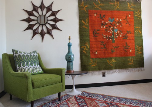 A midcentury living room decorated with a tapestry, chair, side table, area rug.