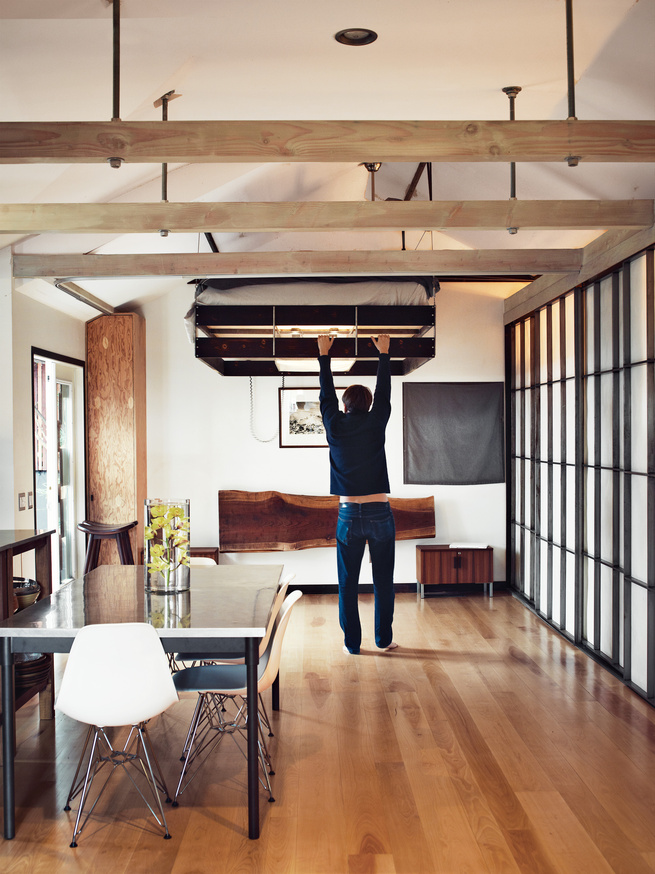 A man is pulling down a bed from the ceiling in a small apartment.