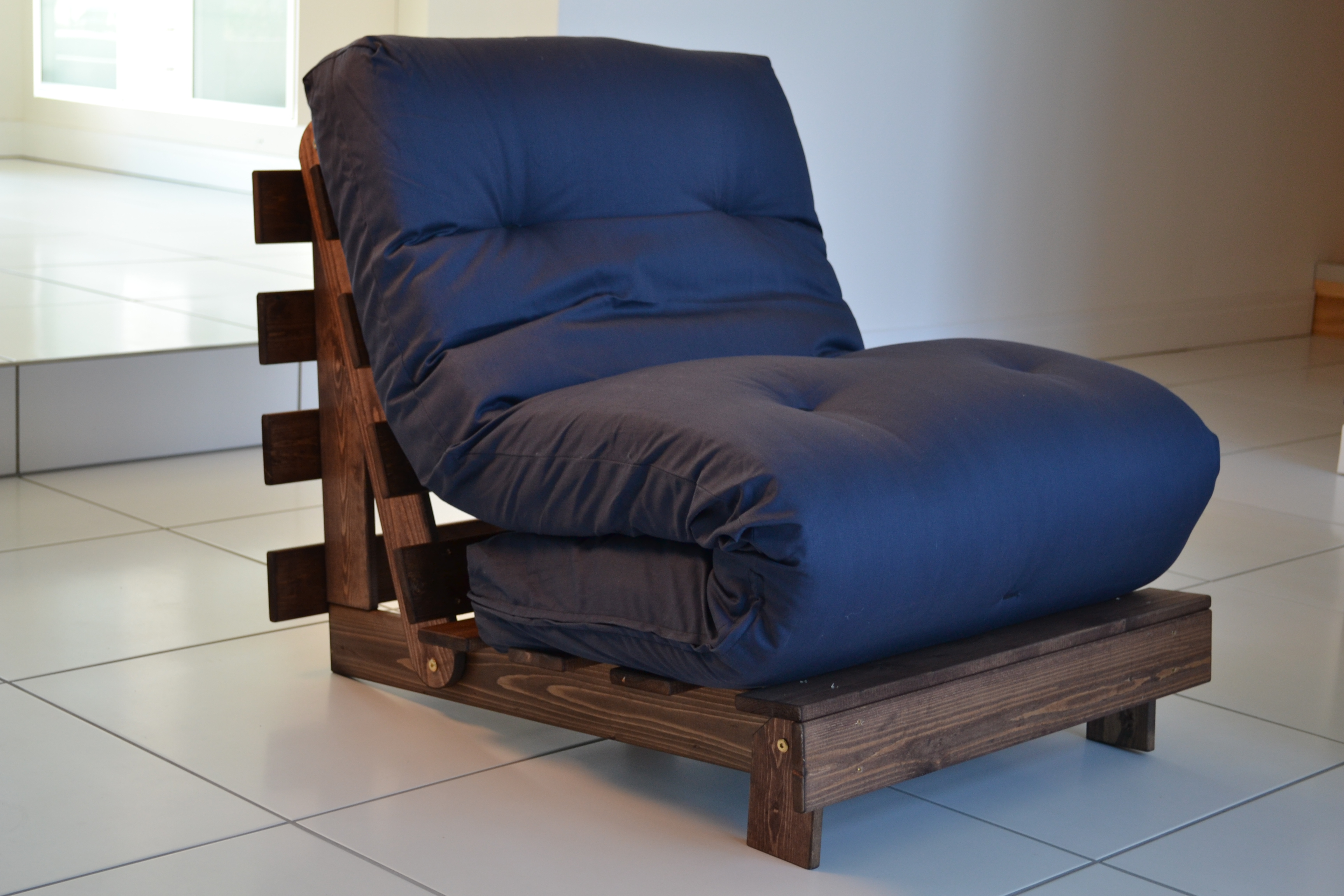 A blue futon folded up onto a brown DIY wood pallet chair.