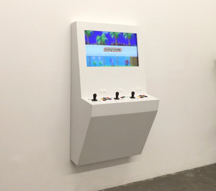 A white Polycade arcade game is mounted to a white wall in a tiny apartment.