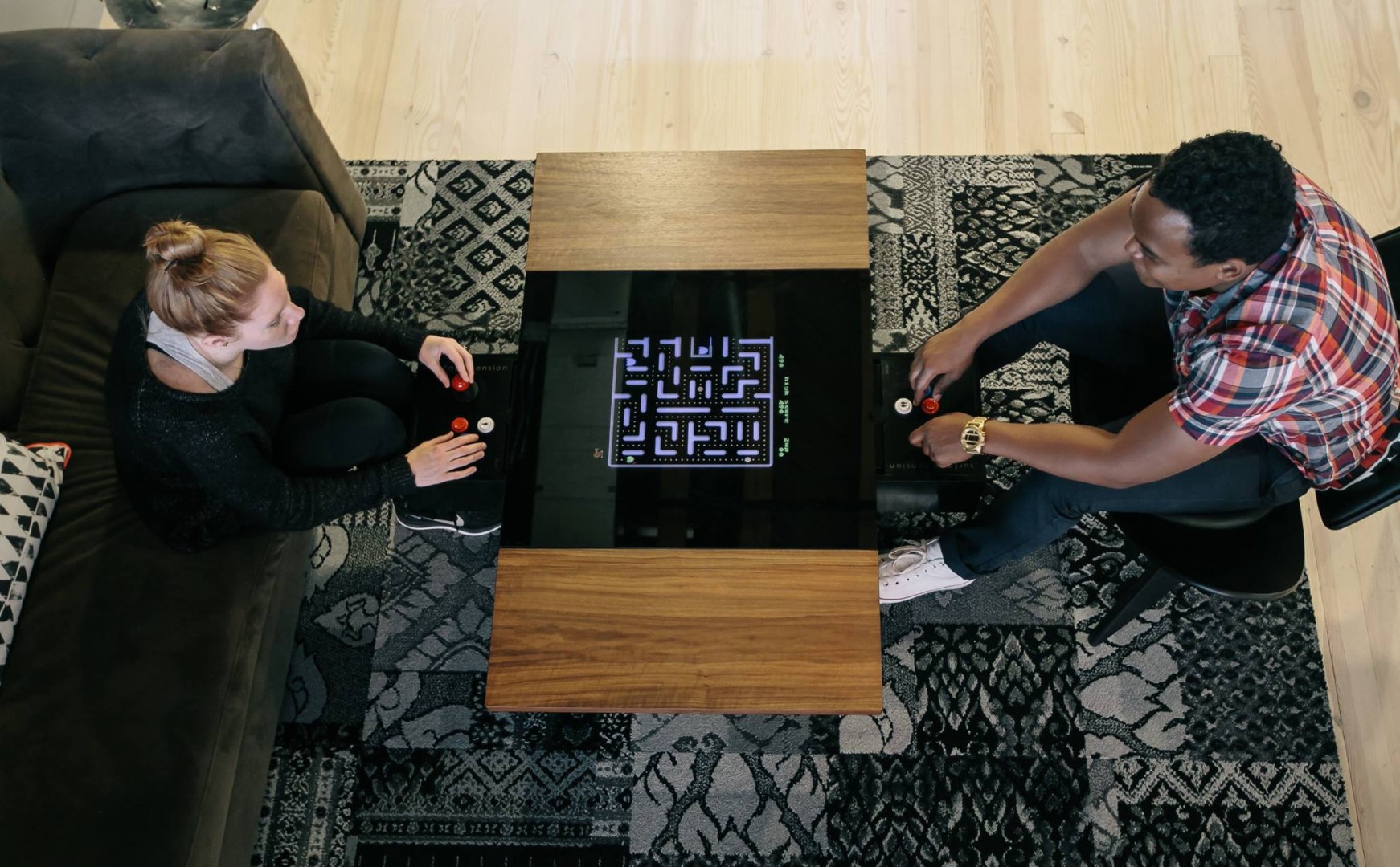 A man and woman playing Surface Tension's Dual Arcade table in a living room.