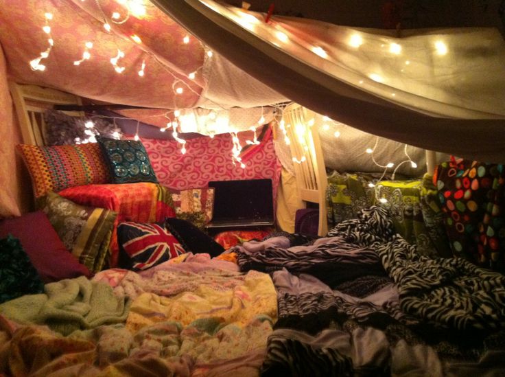 A cozy blanket fort with pillows, string lights, and a laptop.