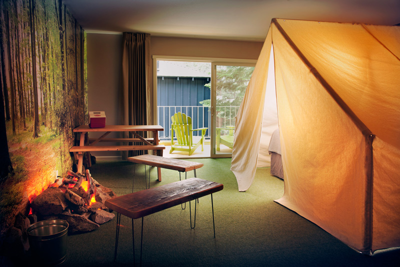 Camp indoors at Basecamp Hotel, which includes a tent, picnic table, benches, an indoor fire pit, and more.